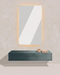A minimalist bathroom scene with a rectangular wall mirror glowing softly from a lighted frame, mounted above a floating dark teal shelf. Small bathroom accessories sit on the shelf against a light textured wall.