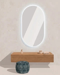 An oval backlit LED wall mirror with a glowing white border, mounted on a textured beige wall above a floating wooden vanity shelf and a round blue-green pouf.