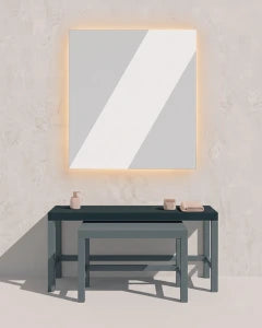 A minimalist interior scene with a large rectangular wall mirror framed in warm light, above a dark console table against a textured light gray wall.