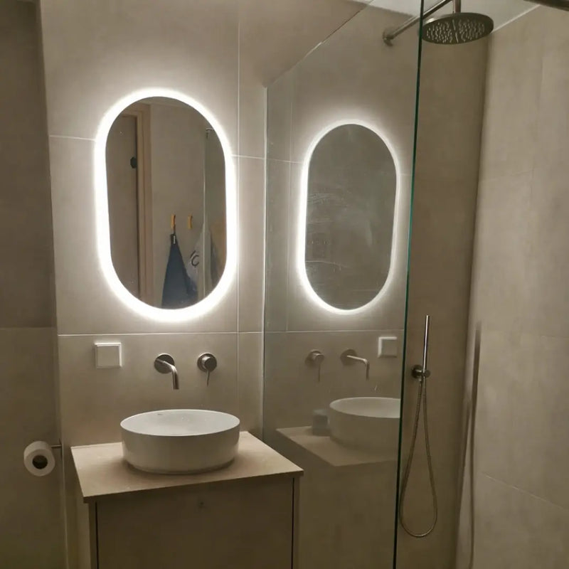 Bathroom with illuminated oval mirror, sink, and shower area.