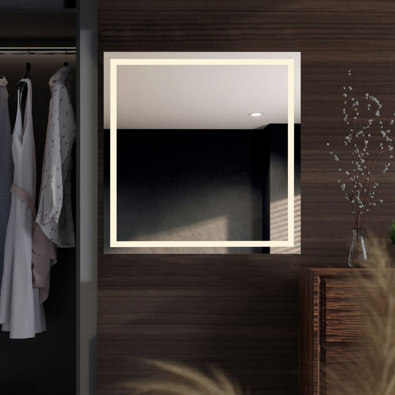 A square LED mirror with double front lighting, mounted on a wooden wall, with a dim reflection of clothes and a vase visible in the mirror.